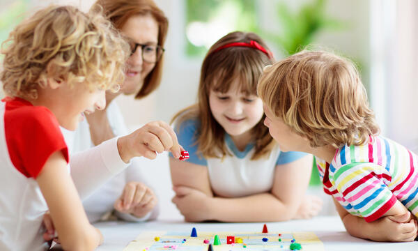 Bild vergrößern: Eine Frau spielt mit drei Kindern ein Brettspiel.