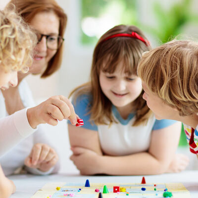 Bild vergrößern: Eine Frau spielt mit drei Kindern ein Brettspiel.